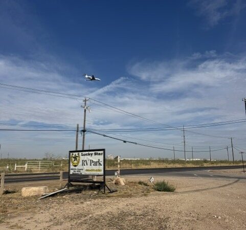 Plane flying low over the Lucky Star RV Park entrance sign on County Road 1270, near Midland International Airport