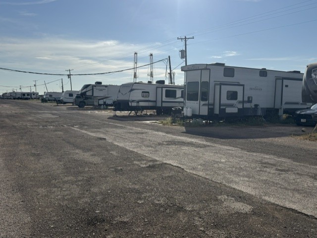 Row of RVs parked along a paved drive at Lucky Star RV Park in Midland, TX, with drilling rigs in the background