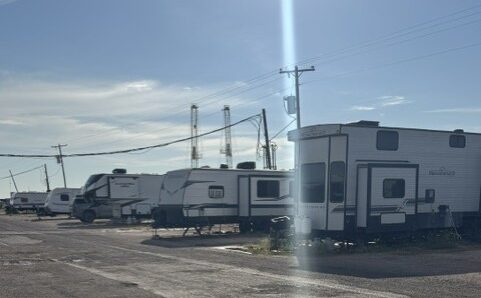Row of RVs parked along a paved drive at Lucky Star RV Park in Midland, TX, with drilling rigs in the background