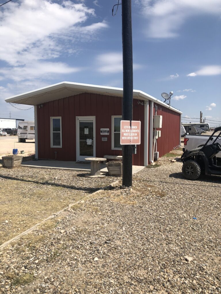 Red metal office building at Lucky Star RV Park in Midland, TX, with a covered porch and RVs parked nearby